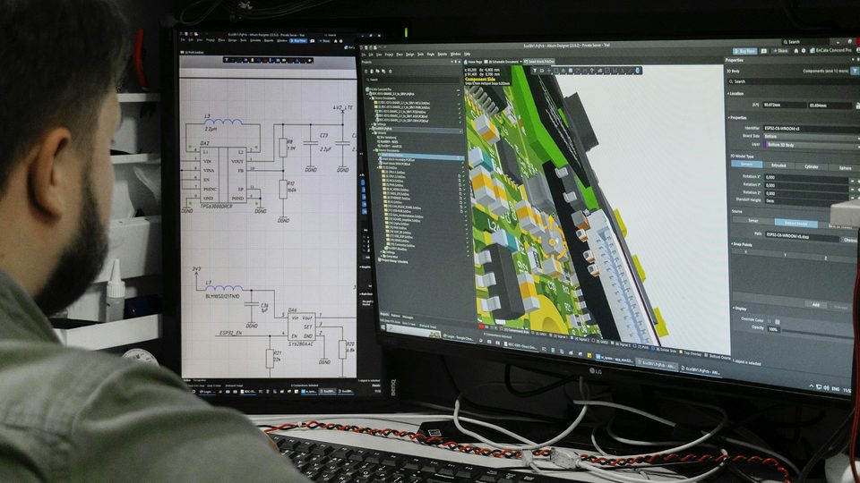 Engineer aan twee schermen met een elektrisch schema en een printontwerp