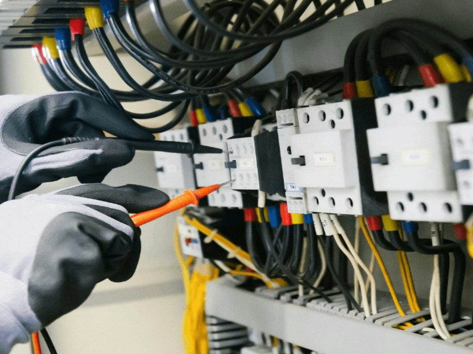 Technieker met handschoenen meet met testpennen aan contactoren in een schakelkast